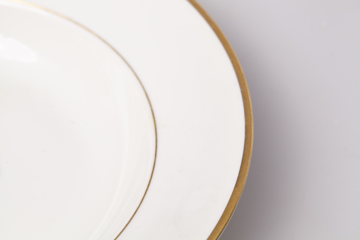 Suppetallerken i hvit porselen. Produsert av Porsgrund Porselen i 1959. Dekorert med gullkant og ring av gull i overgangen til mansjetten. 