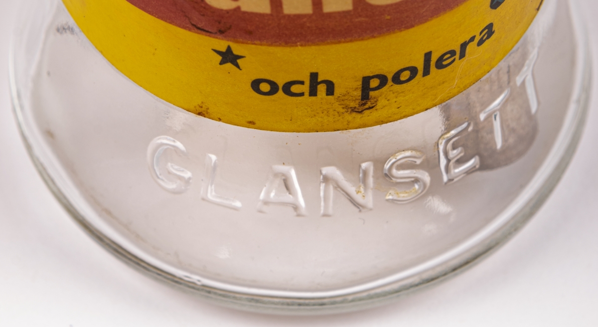 Glasflaska med pump av metall. Gul etikett men texten "Glansett". Har innehållit putsmedel till blanka ytor som glas och kakel.