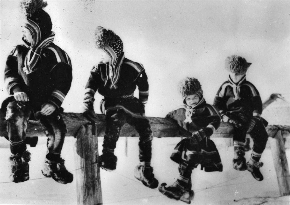 Fire samiske gutter sitter på en stokk.