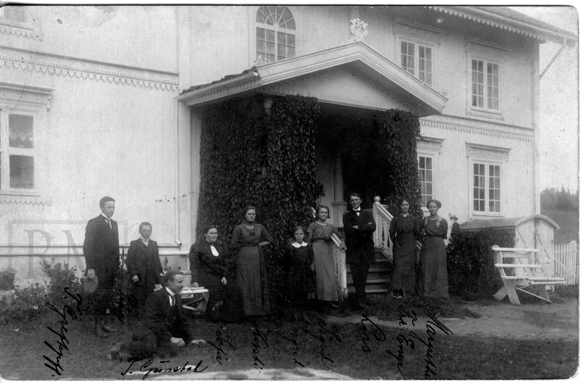 En større gruppe, familien Olimb med flere, samlet utenfor et stort våningshus
