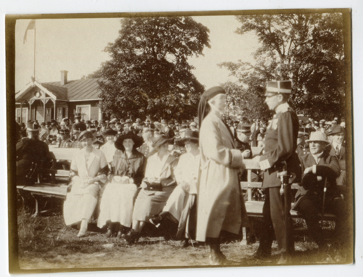 Malmen 3/9 1922. Några civilklädda kvinnor,män och
militärer sitter på långa bänkar i Malmslätt.
