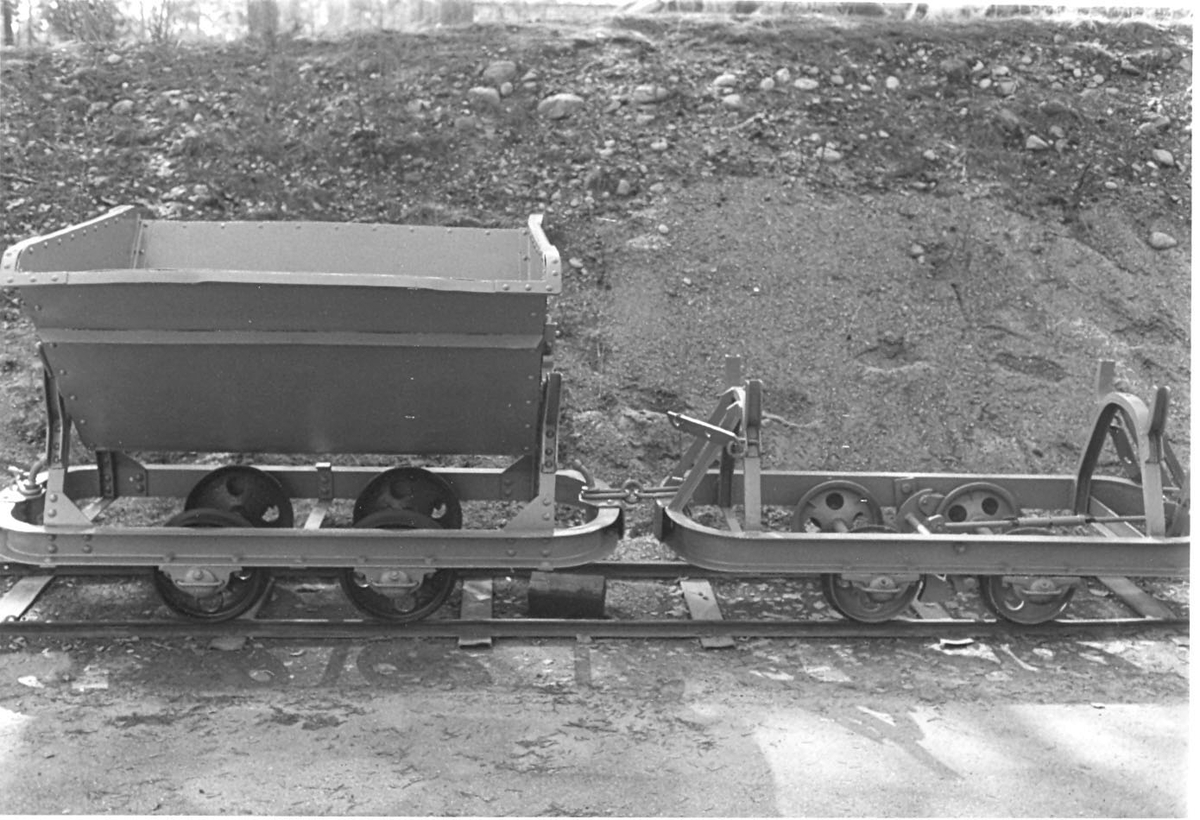 Gråmålad tippvagn eller décauvillevagn (efter den franske uppfinnaren Paul Décauville, 1846-1922), på ram med fyra hjul för rälskörning. Vagnskorgen med spetsig bas, upphängd så att den kan tippa åt båda håll. Dragkrok med kedja i ena änden.
På samma accessionsnummer finns ett ensamt underrede till liknande vagn.  Stående på en rälsbit, med slipers av järn. Rälsens längd 5100, spårvidd 650.