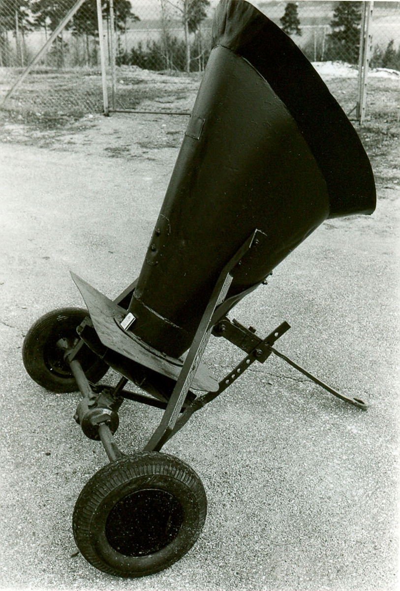 Trattformad sandspridare av plåt, grönmålad. Med två gummihjul.

Typ: SS 
Reg.nr 3992461C