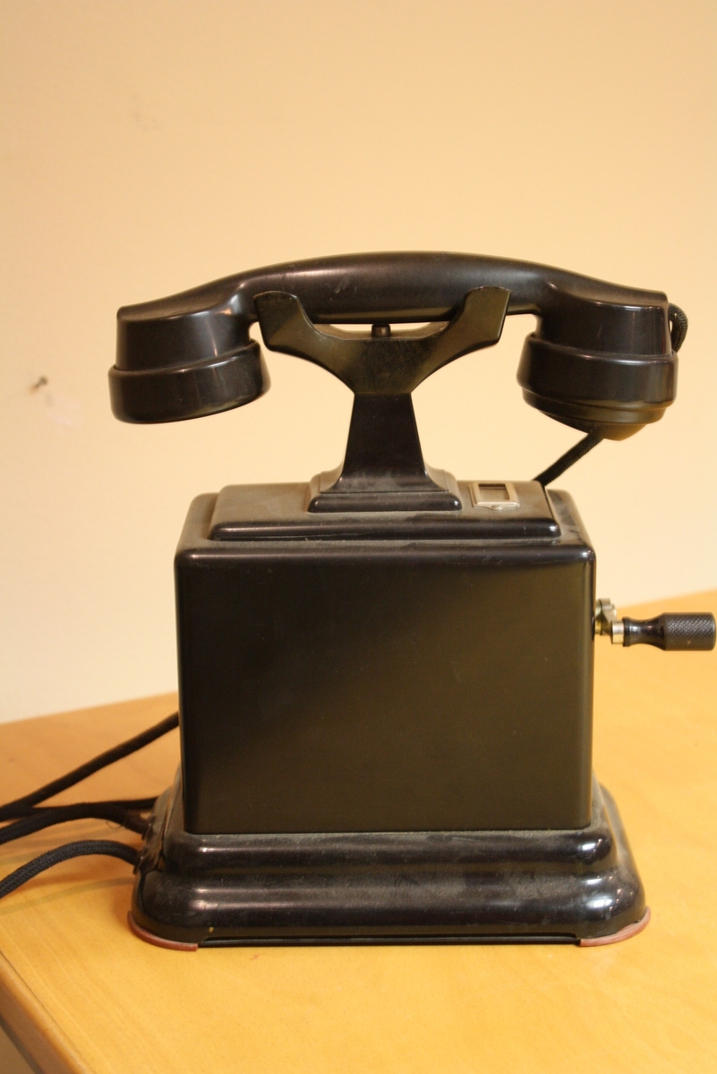 Bordstelefon i bakelit och svartlackerad plåt med vev.
+Planch över Telegrafverkets Telefonapparater 1939