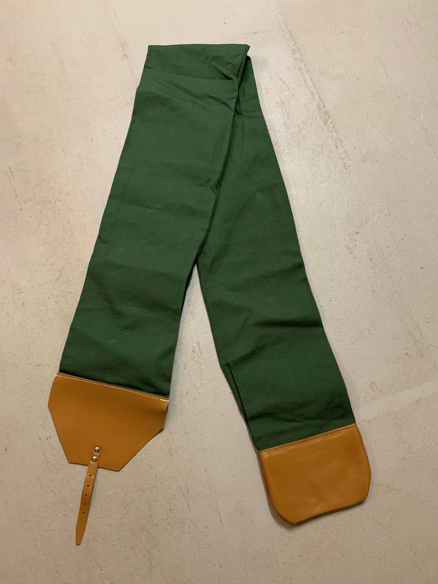 Fodral för fana av grön textil
Förstärkning av ljusbrunt läder i ändarna. Öppning med metallspänne