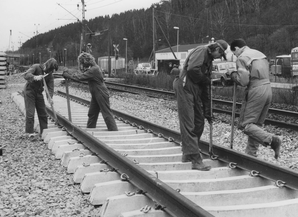 Utbyggnad för pendeltåget 11 april 1990. Vy norrut på män som utför utläggning av nya järnvägsspår, Torrekulla i Kållered. Till höger ses Långåsen samt fastigheter utefter Gamla Riksvägen.