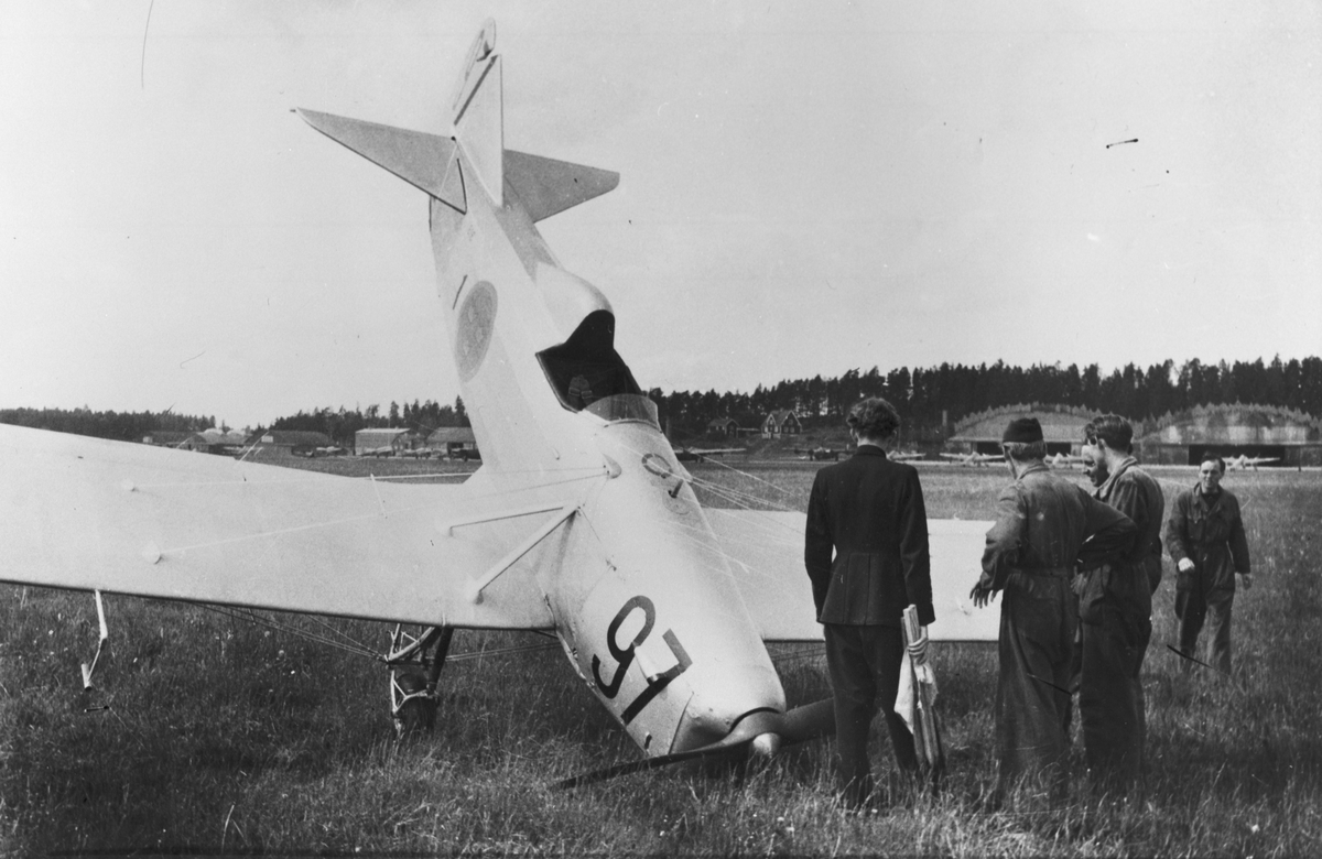 Provflygplan P 1 Sparmann nummer 816, märkt 1-97 efter haveri på flygfältet på F 1 Hässlö, Västerås. Flygvapenpersonal vid flygplanet. Berghangarer i bakgrunden.
