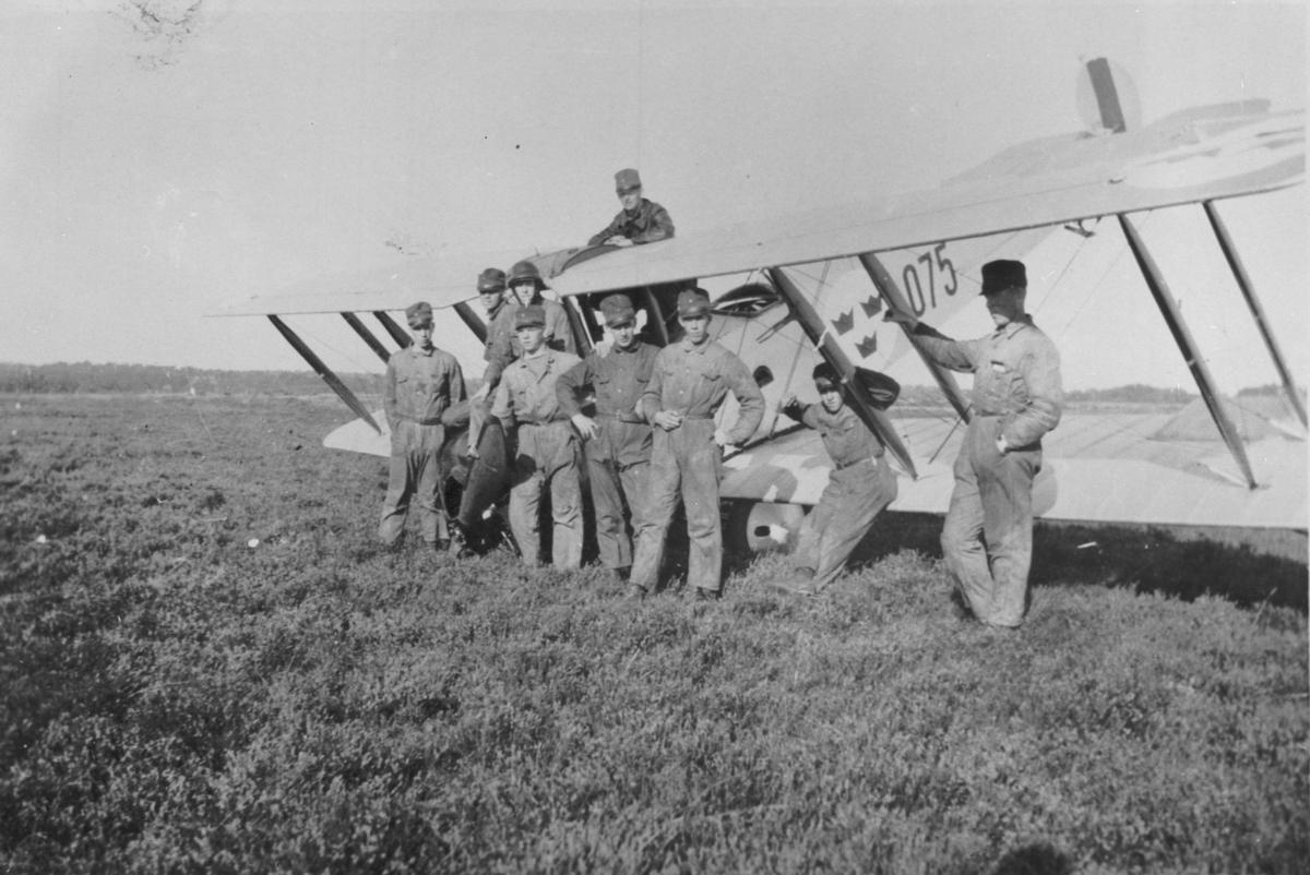 SK 3 Avro 504K Mk 2 märkt 075 står på nosen på ett flygfält på Ljungbyhed, där den var i tjänst 1927-1928, innan totalhaveri 5 mars. 9 militärer kring planet.