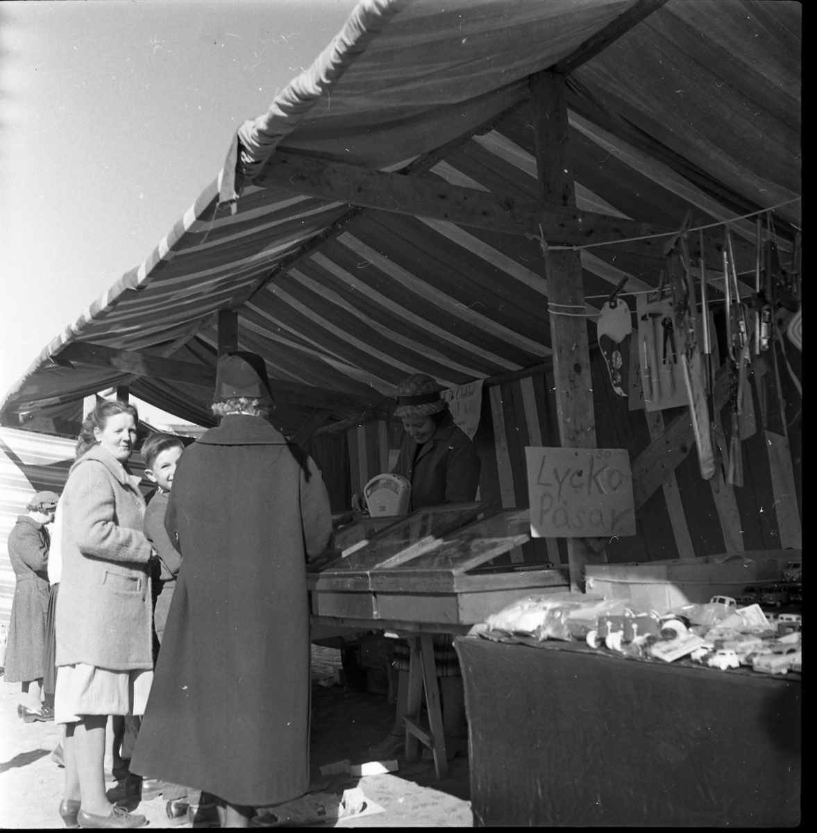 Två kvinnor och en pojke står och handlargodis i ett marknadsstånd. Kvinnan bakom disken väger godiset på en våg.