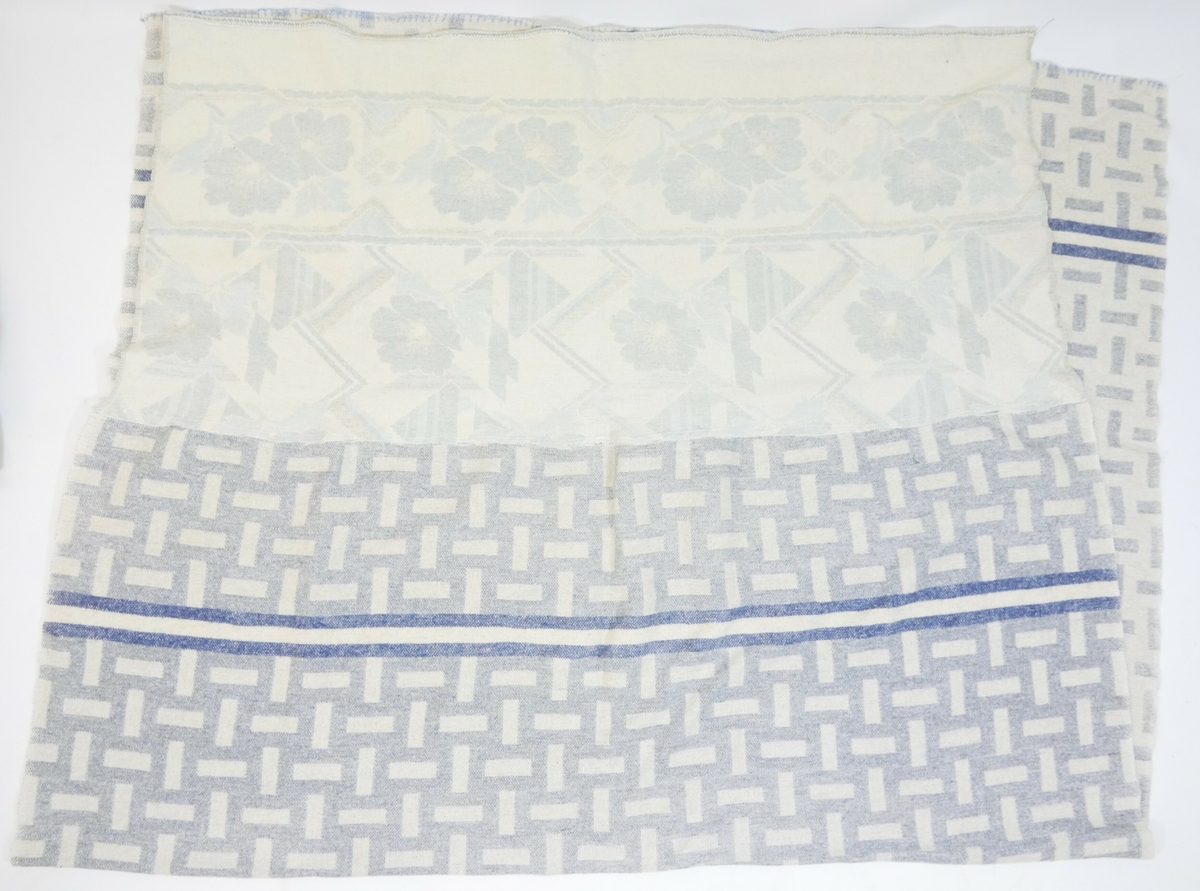 Rektangulært pledd med mønster i hvitt og blått. I den enen enden er det påsydd ett nytt tekstilstykke som har hvit bunn med blomstermønster i blått. 