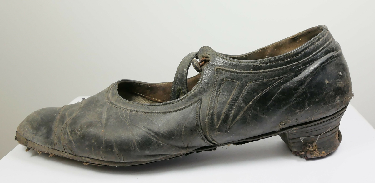 Ett par svarte sko med en hæl og reim. 