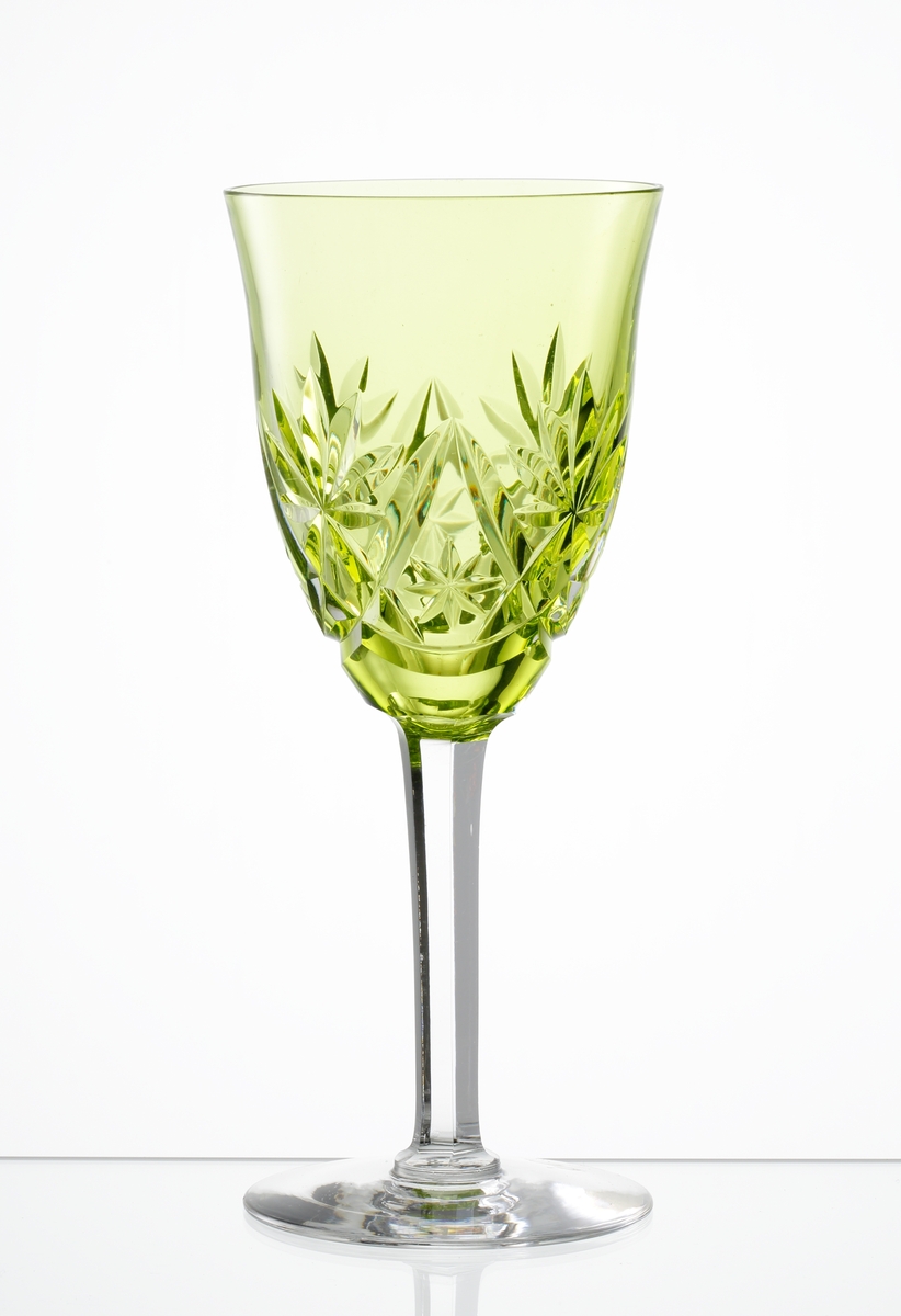 Design: Okänd. 
Vitvinsglas, vid klockformad, gulgröntonad kupa med skärslipad dekor. Facettslipat högt ben med slät fot.