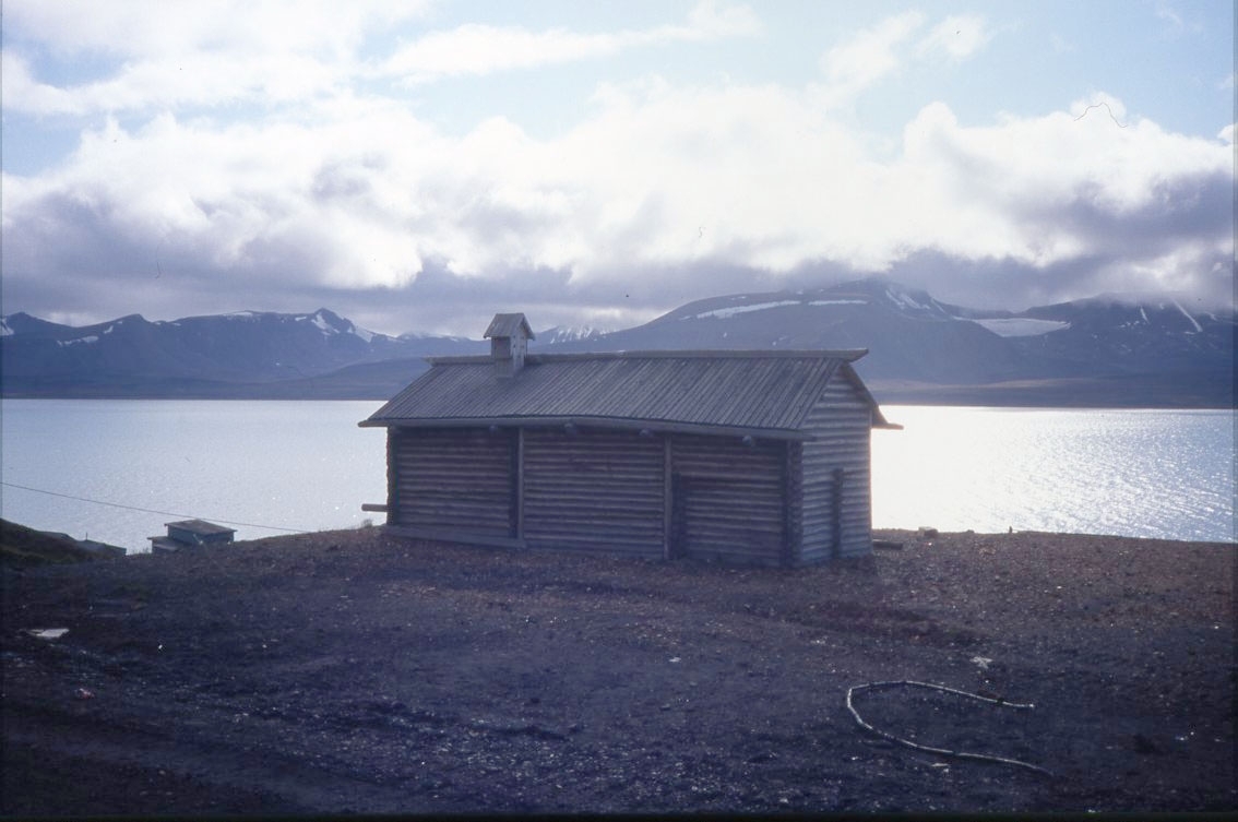 En liten obehandlad knuttimrad byggnad i det ryska gruvsamhället Barentsburg på Svalbard. I bakgrunden syns Isfjorden.