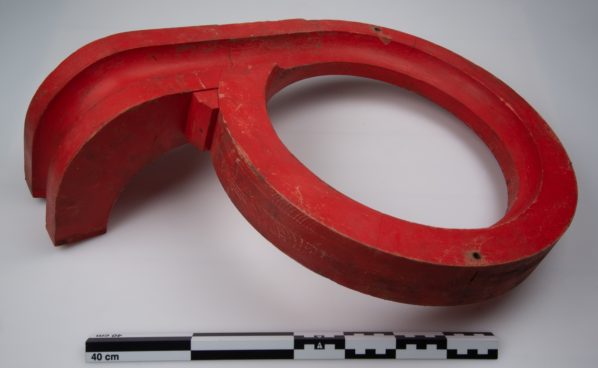 Støpemodellen i tre er malt rød. den består av en ring som går ut i en tut. tuten i seg selv har en bøy som går 90 grader på ringen.  i denne tuten er det utsjært en kanal.
