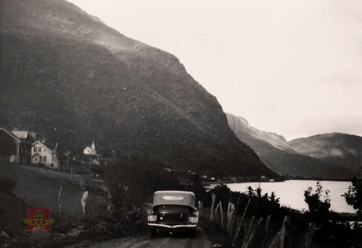 Riksveg 5 ved Ølmheim med kyrkja i bakgrunnen år 1937. 

Ein 1934-modell Buick Kabriolet rutevogn frå Sogn Billag med kjenneteikn S-135 på veg mot Sogndal.

