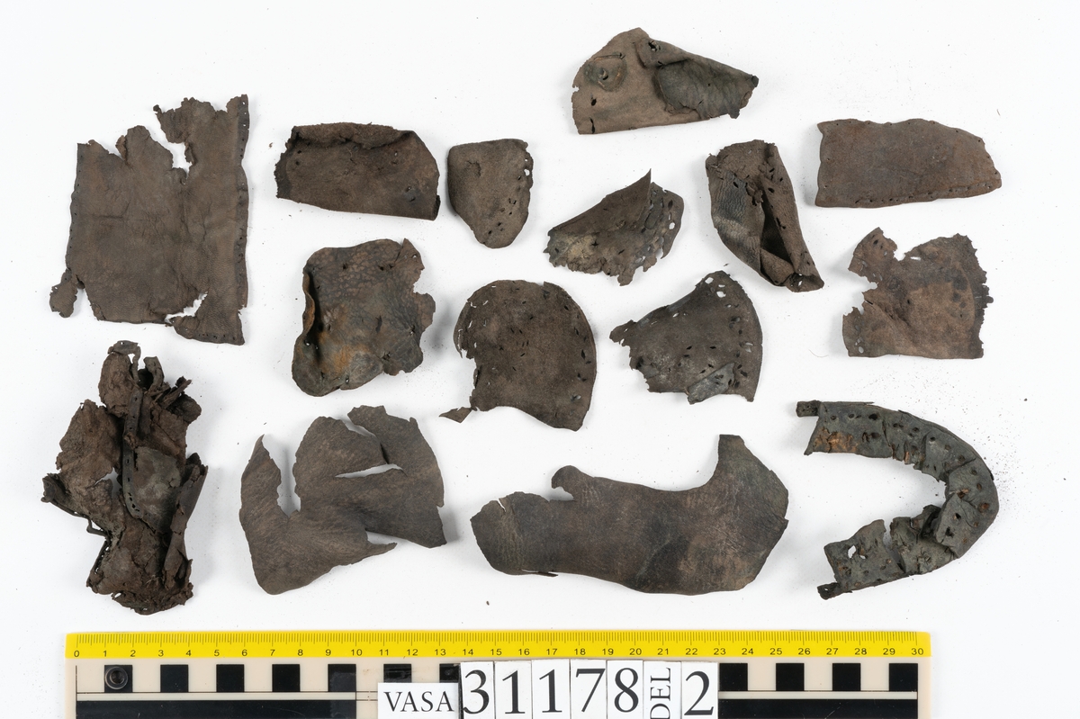 Runt 400 delar och fragment från skor i form av sulor, inlägg, ovanläder, klack, sidostycken, bakkappor, träpliggar, tråd mm. Troligtvis rör det sig om delar och fragment från flera skor och/eller stövlar. Delar av lädret har förstärkts med lim av konserveringsenheten. Merparten av lädret är spaltat samt har hål efter träpligg eller stygn.