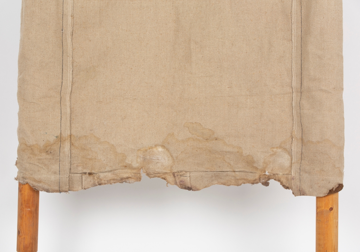 Rektangulært bærestykke av seilduk, langsgående lomme på hver side. Stropper og maljer på ene kortsiden.  Bærestenger av løvtre. Det følger med 2 sett sengebein.