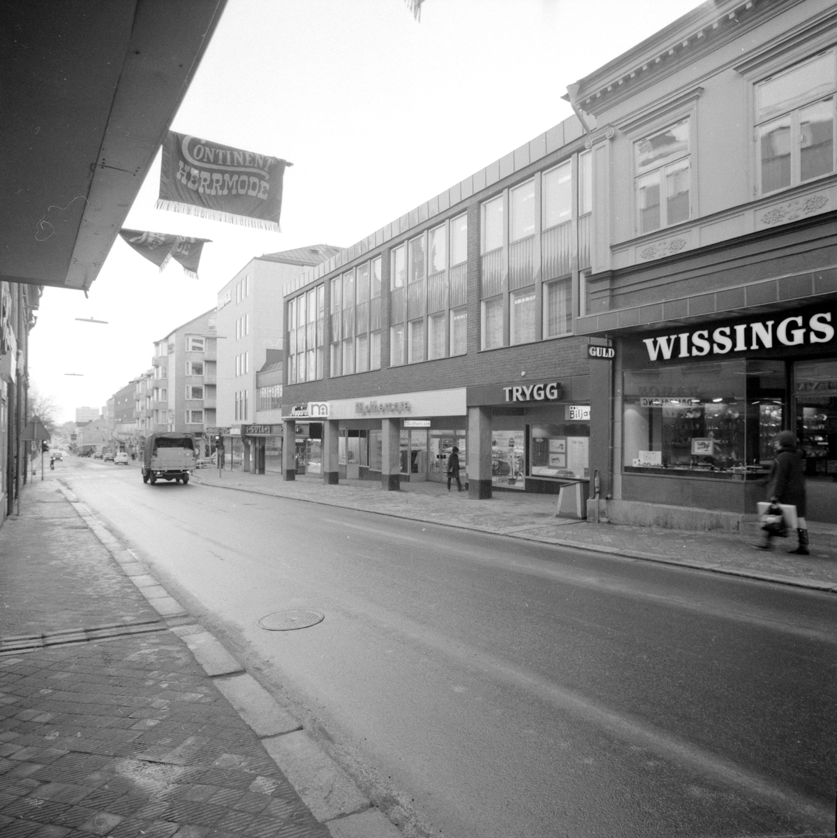 Vardagligt motiv från Storgatan i Linköping. Tiden är en vårvinterdag 1971 och byggnaderna i blickfånget är nyligen färdigställda. Bland butikerna återfinner vi ett nymodigt inslag i Mothercare från den brittiska butikskedjan med samma namn och som specialiserats sig på artiklar för blivande föräldrar.