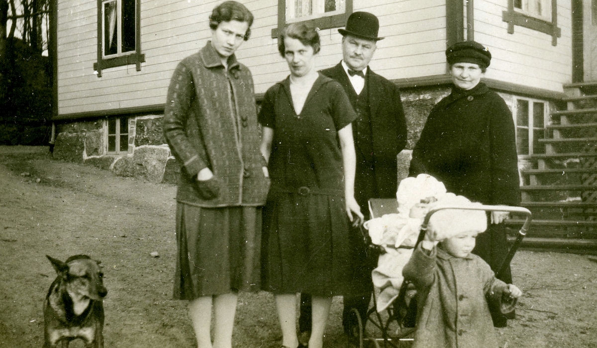 Systrarna Astrid (1907 - 1994, gift Jägerström, Råda) och Ingeborg Gustafsson (1901 - 1987, gift Johansson) står tillsammans med två små barn, ett äldre par och en hund utanför Kållered Stom "Nygård", okänt årtal.