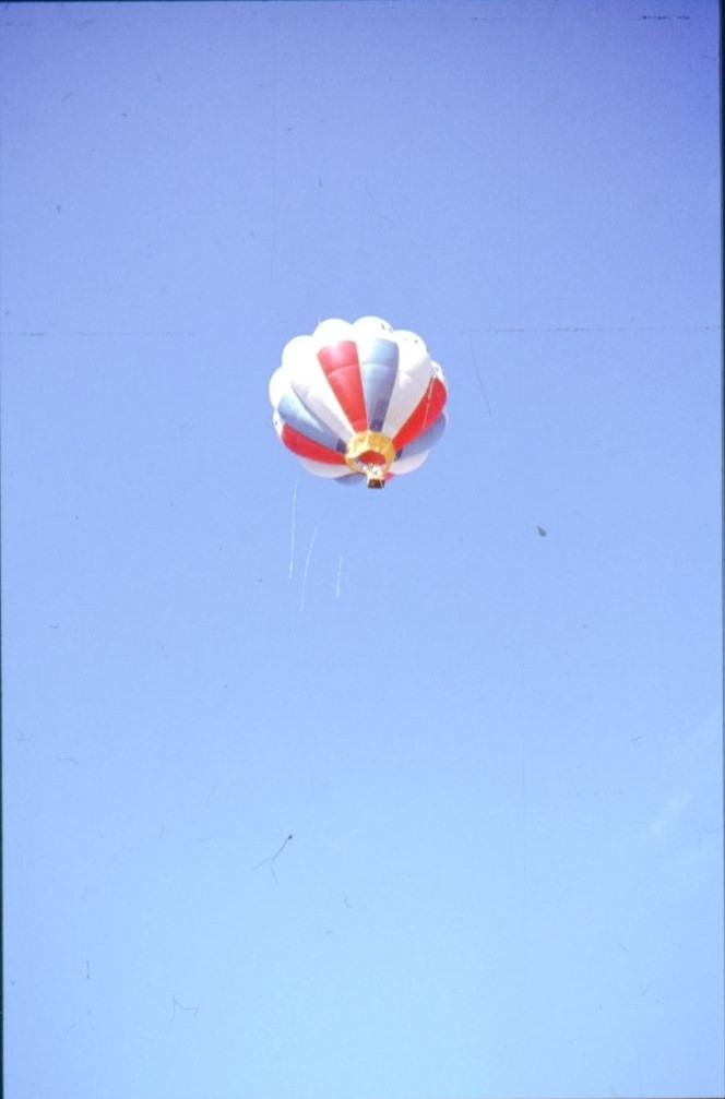 En röd-blå-vit ballong, möjligen märkt "KORAL" i luften. Fotograferad nästan rakt underifrån.