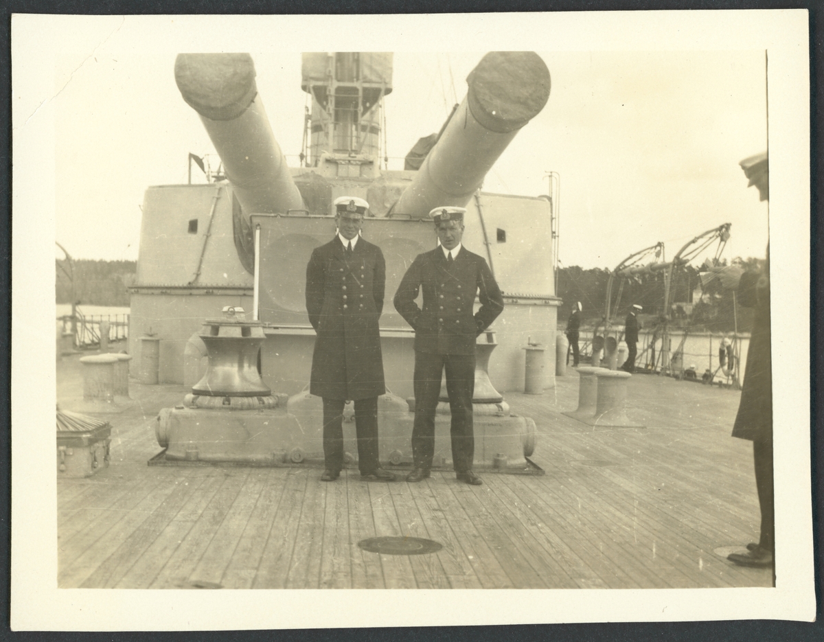 Bilden visar två sjöofficerare som står på däck av pansarkryssaren fylgia under kanonerna.