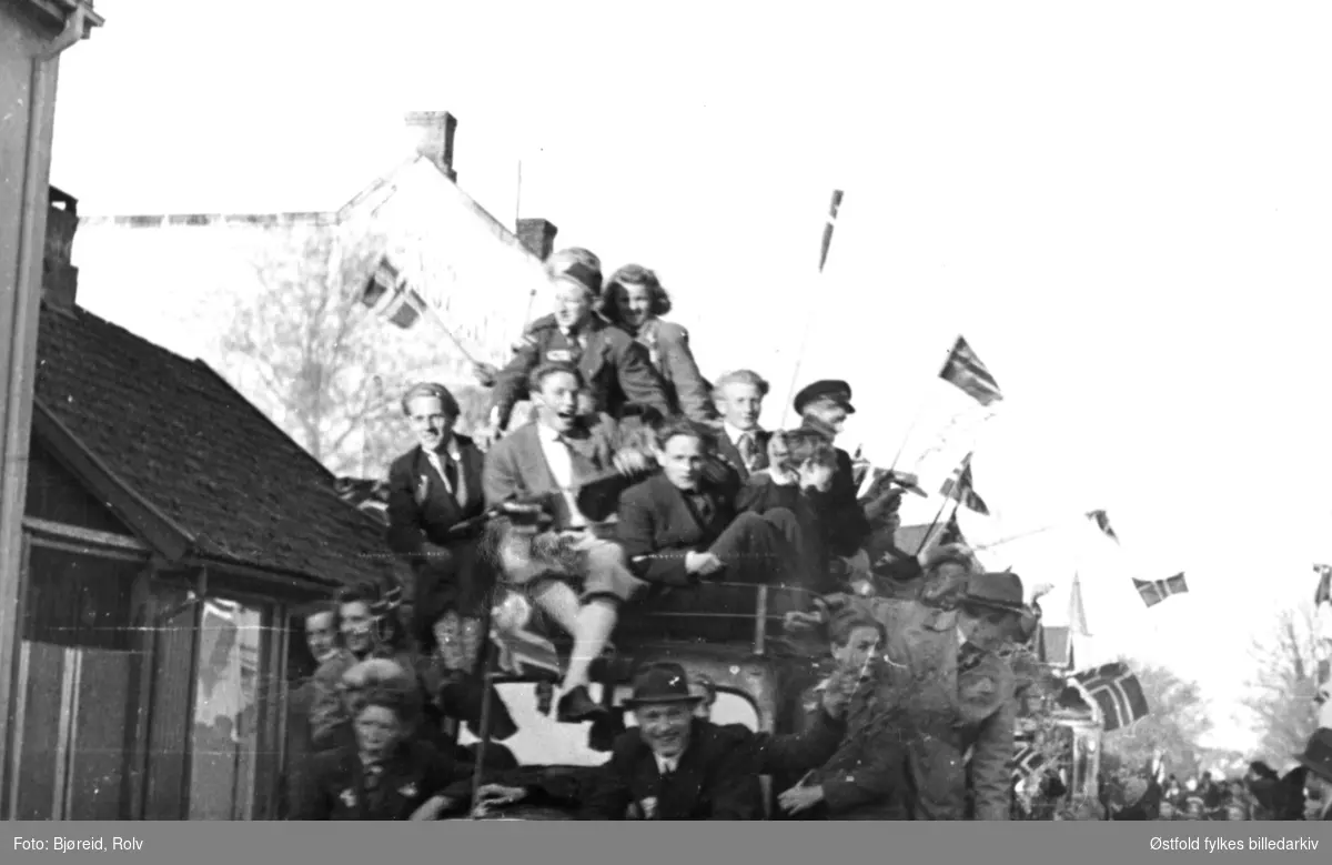 Da freden "brøt løs" i maidagene 1945. Fra Torvet i Sarpsborg.
Jublende menneskemengde med flagg på lastebilplan, del av tog.
Foran en Ford V8 1937 lastebil.