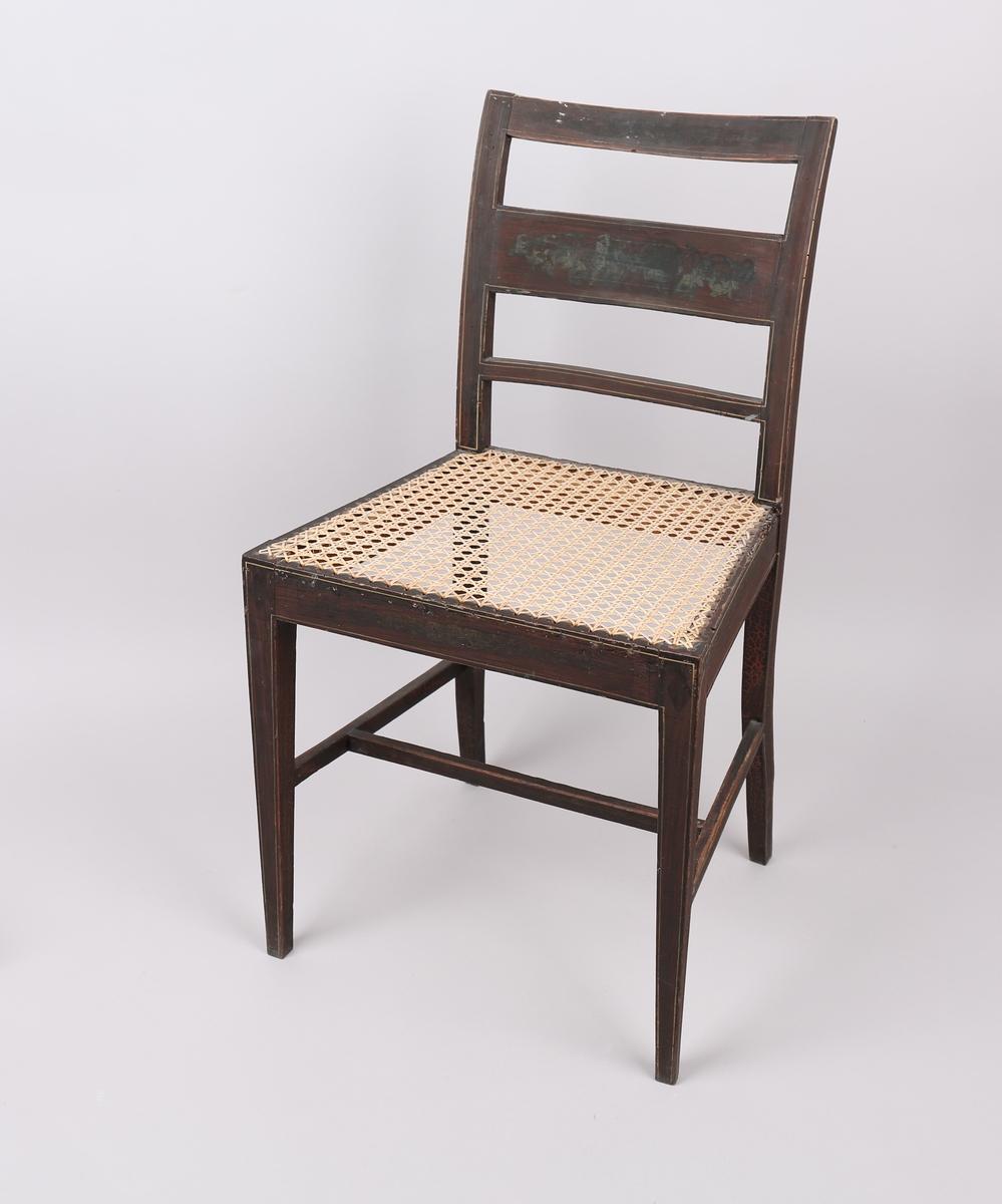 Enkel stol med rottingsete og en dekormalt ryggplate i midten. Gylne kantlinjer malt langs sarg og ryggplater.