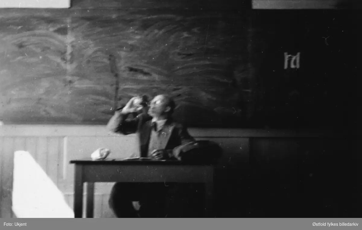 Klasserom i Fredrikstad, H-7 merke på tavla 17. mai 1940. Ukjent lærer eller lektor sitter bak kateteret.