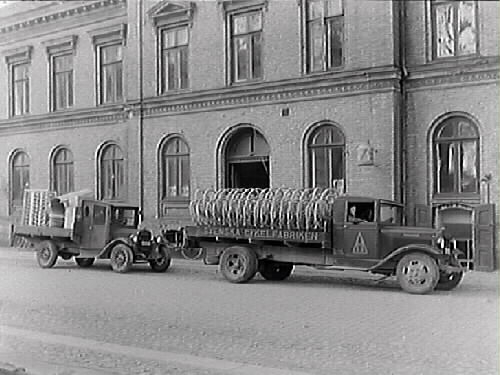 En större lastbil, "Svenska Cykelfabriken", med cykelhjul på flaket samt en mindre vid Rommelska fastigheten i Varberg. (Svenska Cykeldepoten bytte 1925 namn till Svenska Cykelfabriken, som i sin tur ändrades till Svenska Cykelfabriken Monark år 1934)