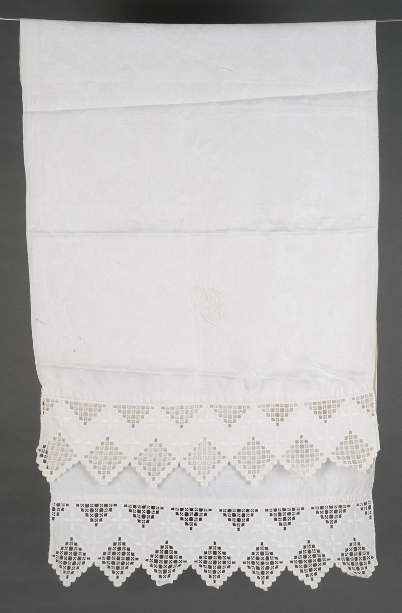 Damaskvevd pyntehåndkle med påsydd dekor av hardangerbroderi. Brodert initialene B i engelsbroderi.