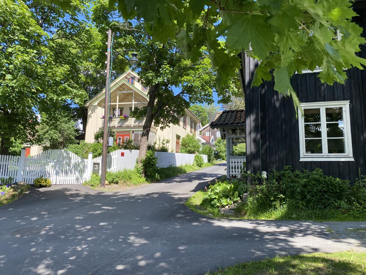 Fotografi av Øvrebyen, tatt på 2010-tallet. Det er sommer og frodig. Man ser to hus i en gate. Det ene er svart, søtt og lite. Det andre er stort, lyst og har fargerike detaljer.
