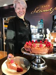 Ansatt i Kafe Standpunkt står bak disken og viser fram en lekker sjokoladekake