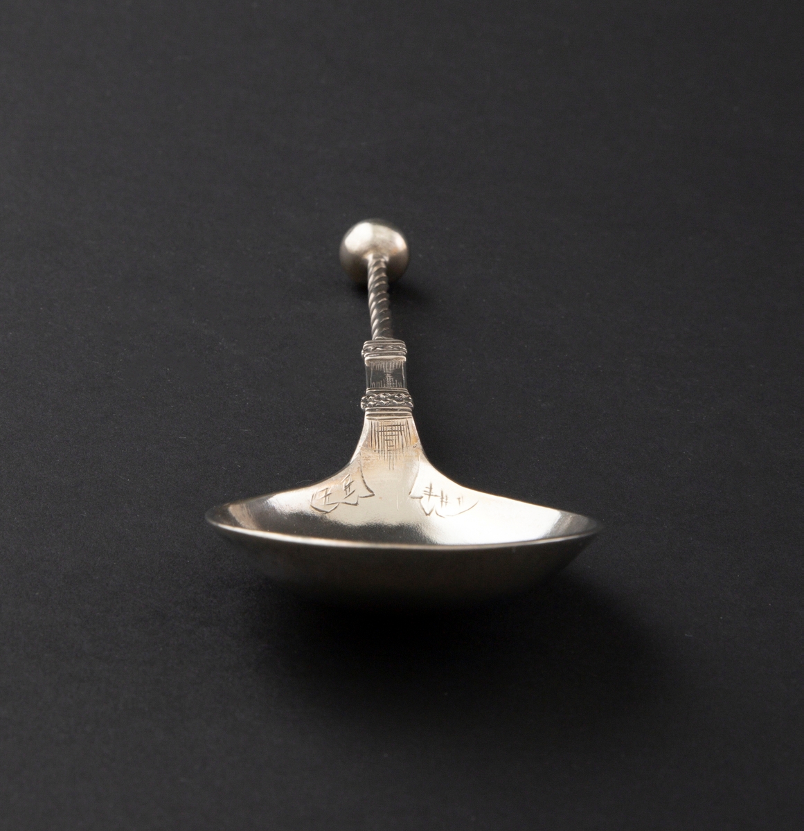 Kuleskje av sølv med dråpeformet skjeblad. Skaftet er flatt nedentil og vridd oventil.