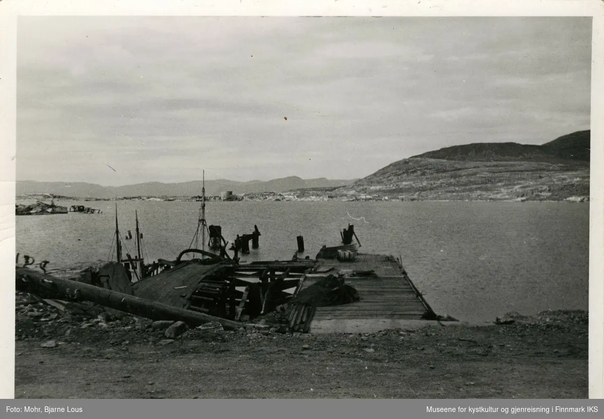 Den ødelagte dampskipskaia i Hammerfest havn etter andre verdenskrig. I bakgrunnen ser man Fuglenes.