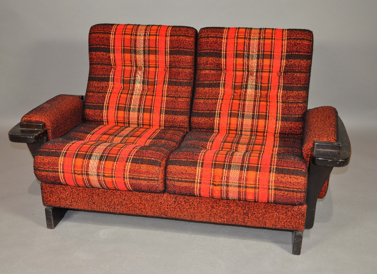 Sofa trukket i brunsvart stoff med rustrød og oransje felt. Treverket er i beiset bøk. Vendbare seteputer.