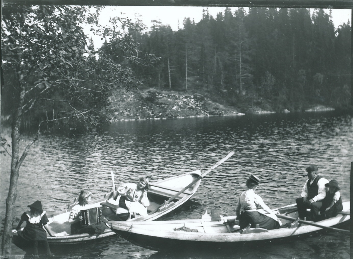 Familien Rydgren i to trebåter på innsjøen nedenfor Mosjøhytta. I den ene båten er tre av Rydgren-jentene, hvorav en med trekkspill, og i den andre båten sitter bestyrer Rydgren, fru Nicoline Rydgren og en av døtrene.