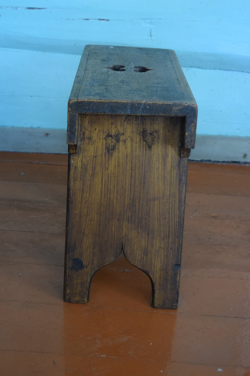 Høybent krakk av furu. 1700-talls. Krakken har to ben laget av to vertikalt stående bordbiter. Sidene på krakken er utskåret i tungemønster. Selve setet har to hjerter som dekorasjon.