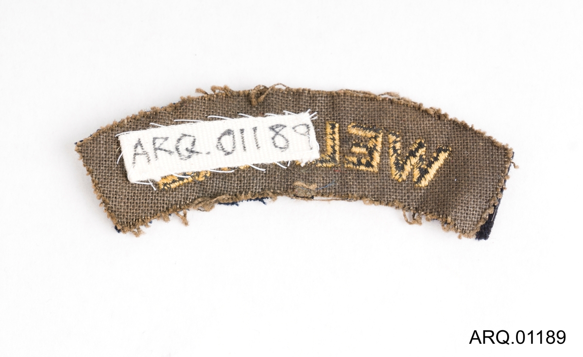 Jakkemerke i tykk filt til å sy på uniformsjakke fra marinen. Svart med skrift brodert med gulltråd.