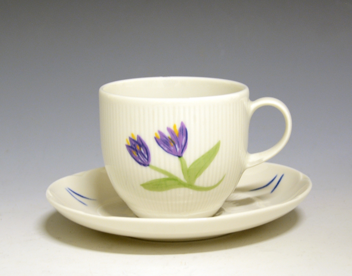 Kaffekopp av porselen med hvit glasur, riller i godset. Dekorert med lilla blomster.
Modell: 2700 Fiore av Eeva Terävä
Dekor: Tidlösa av Ulrica Hydman-Vallien