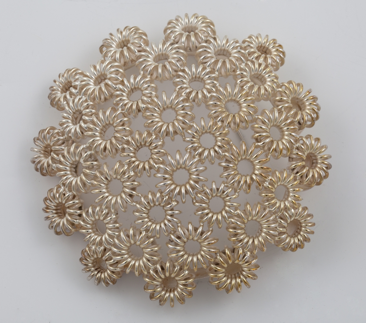 Rund buet brosje i sølvfiligran, bestående av runde stiliserte blomsterformer.