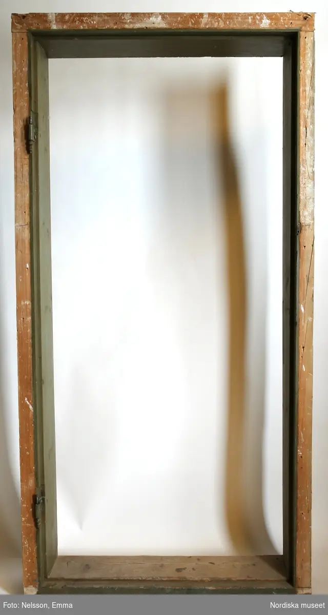 a) Enkeldörr med b) karm, av furu, målad i grågrön oljefärg, omkring 1740. Tre fyllningar med upphöjt mittparti och profilerad list, lika på båda sidor. Skjutvred, beslag och gångjärn. 

Anm: Partiellt färgbortfall och skador. Mittersta fyllningen med kraftig lodrät spricka. 4 st hål, sannolikt efter kammarlås. Dörren har varit placerad på rummets ena långsida. Se tillhörande dörrfoder (NM.0334555a-c).
/Anna Arfvidsson Womack 2021-07-16