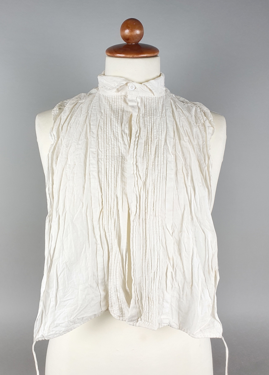 Hvit skjortekrage av bomull med smal krage og vertikale legg langs åpningen midt foran. Lukkes med knapper midt foran og snor nederst på skjortebrystet til å knyte bak.