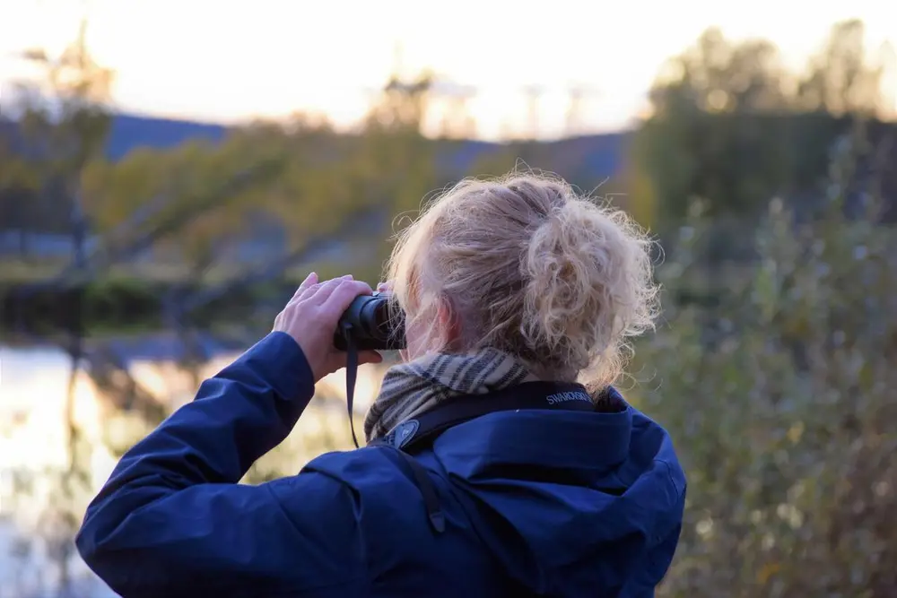 Foto av en kvinne som ser i kikkert utover Glomma