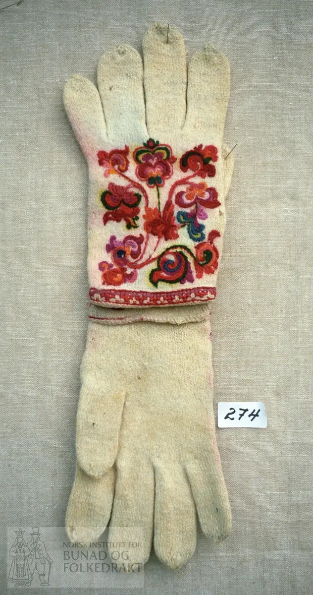 Kvitt heimespunne ullgarn glatt strikka med rosesaum i fleire fargar.  Liten nedbretta krage prydd med korssting og kontursting.