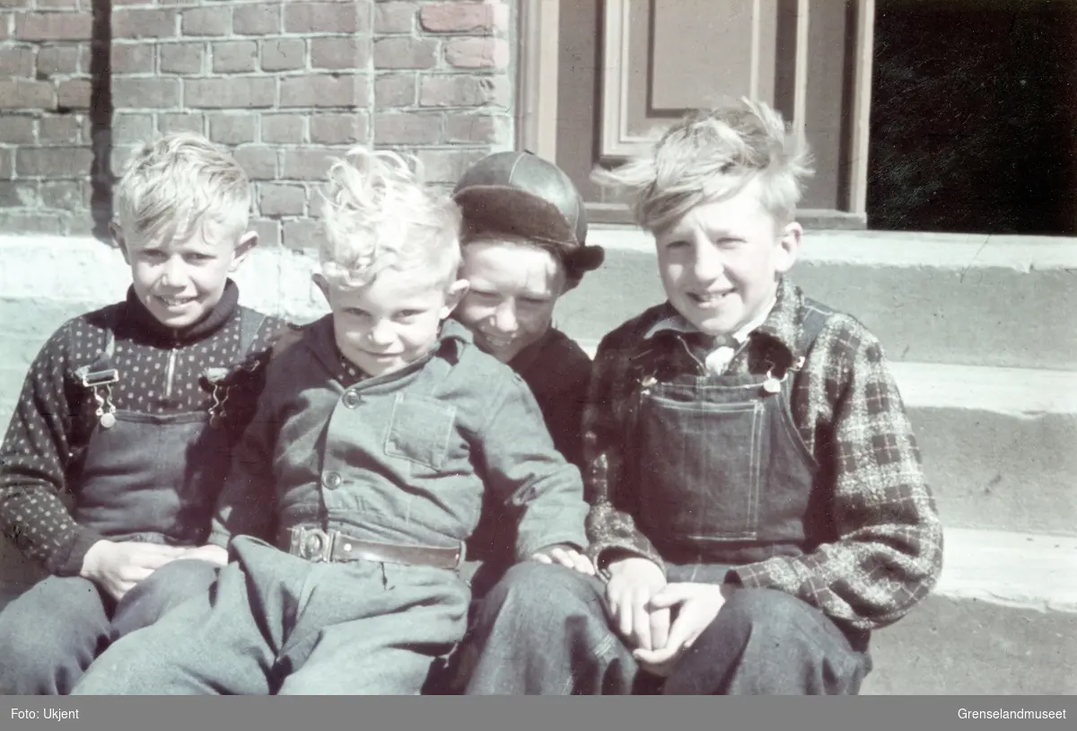 Fem unge gutter sitter på en trapp foran et murhus. . 