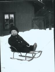 Wilhelm Fredrik Rydgren sitter på kjelke i snøen på gårdspla