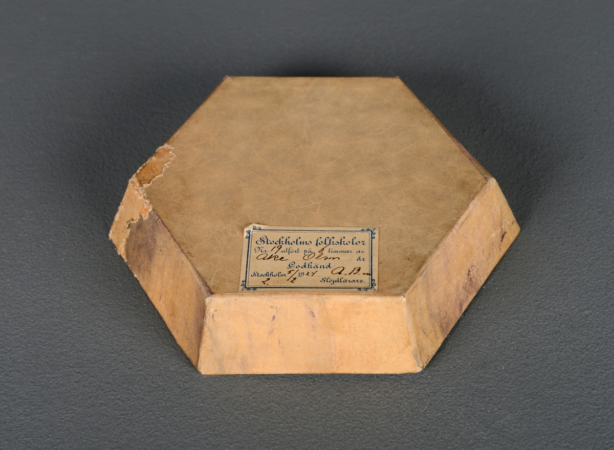 Et håndlaget sekskantet fat av papp som inneholder til sammen 22 puslespillbiter. Det er deler av to forskjellige puslespill og noen deler mangler fra begge to. Laget i 1924 av en elev i pappsløyd.
