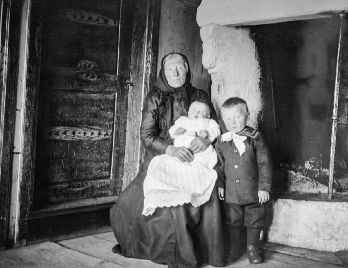 En eldre kvinne med to små barn foran en stor grue
