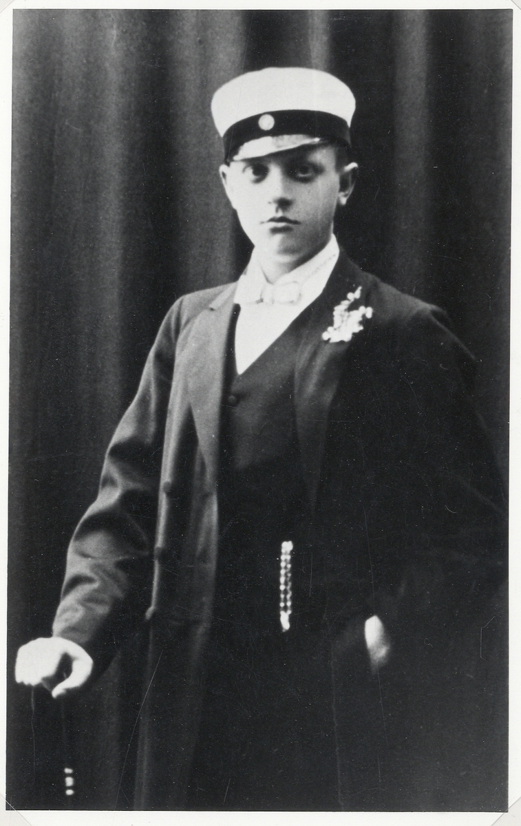 En ung man i bonjour med väst och stärkkrage. På huvudet en studentmössa.
Knäbild, halvprofil. Ateljéfoto 1910.