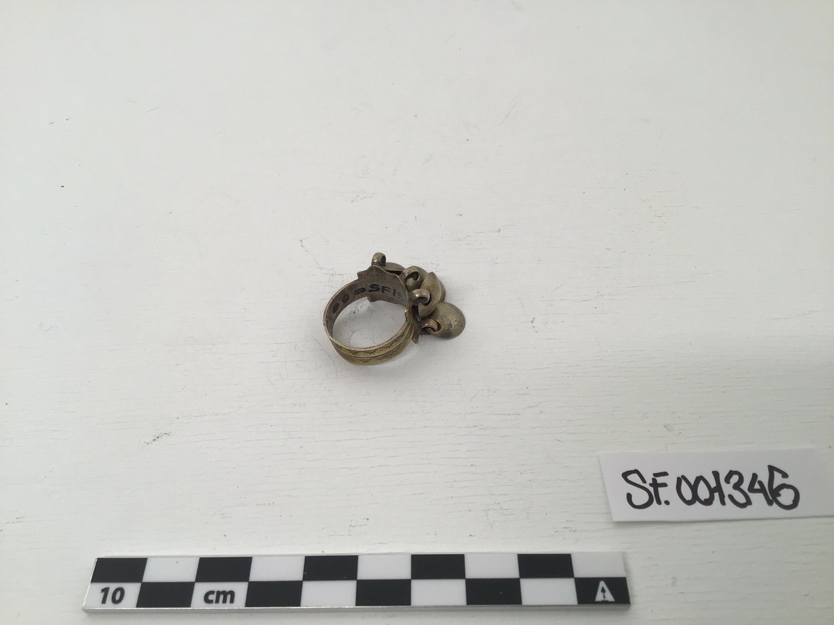 Ringen er av sølv men gylt. Profilering langs kant og sikksakmønster. Ringen er breiare i front og her er kanten takka, som ei krune. Seks skåler(lauv)